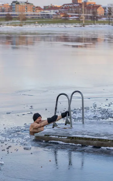 Man climbing into a hole cut in lake ice for a cold plunge