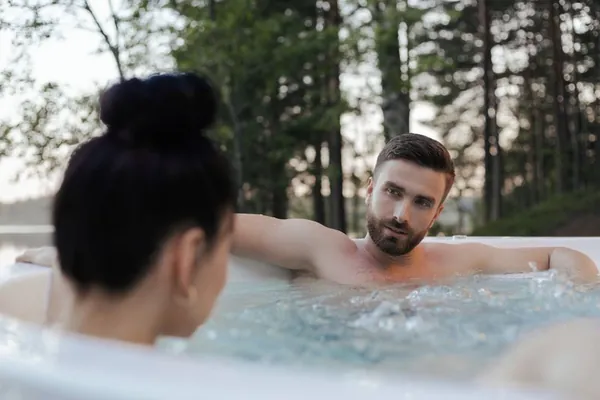 Couple relaxing in an outdoor hot tub surrounded by trees